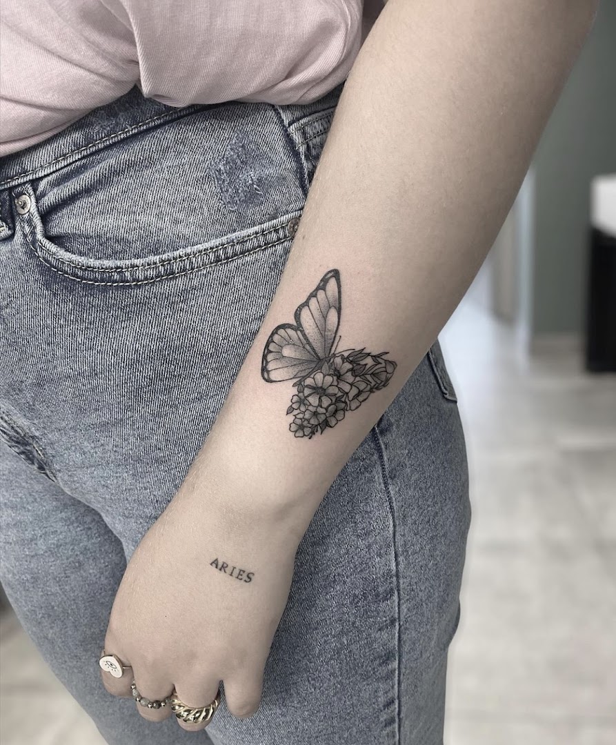 Fijne fine-line tattoo van een vlinder met bloemen op een onderarm