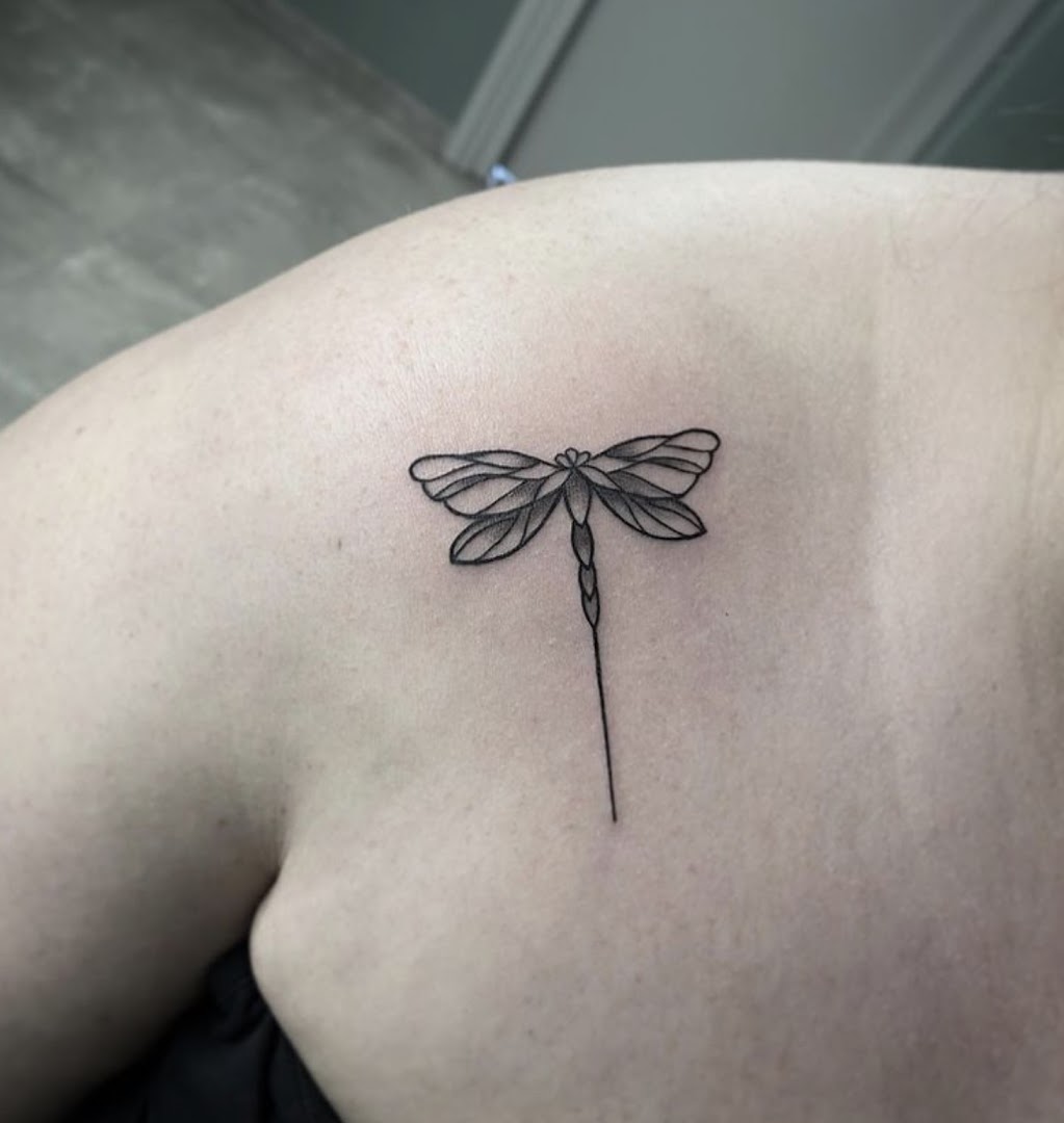 Fine-line tattoo van een libelle op een schouderblad