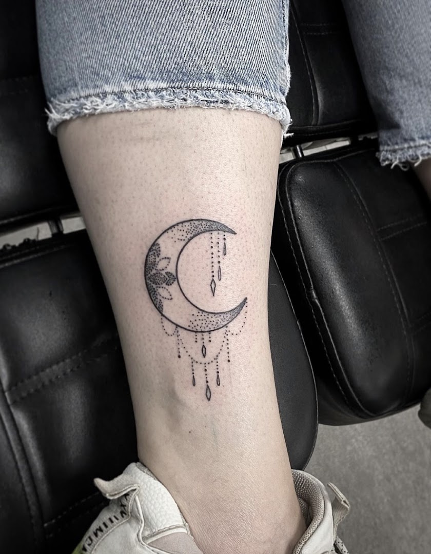 Sieraad-stijl tattoo van een maan met hangende kralen op een onderarm